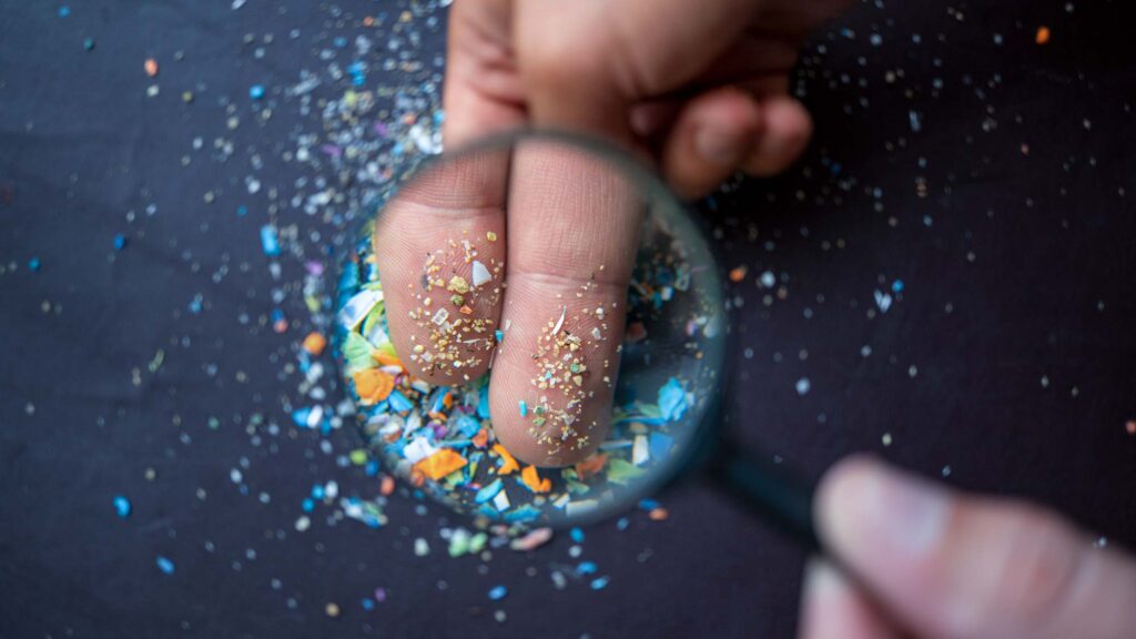microplastics on fingers highlighted by magnifying glass.